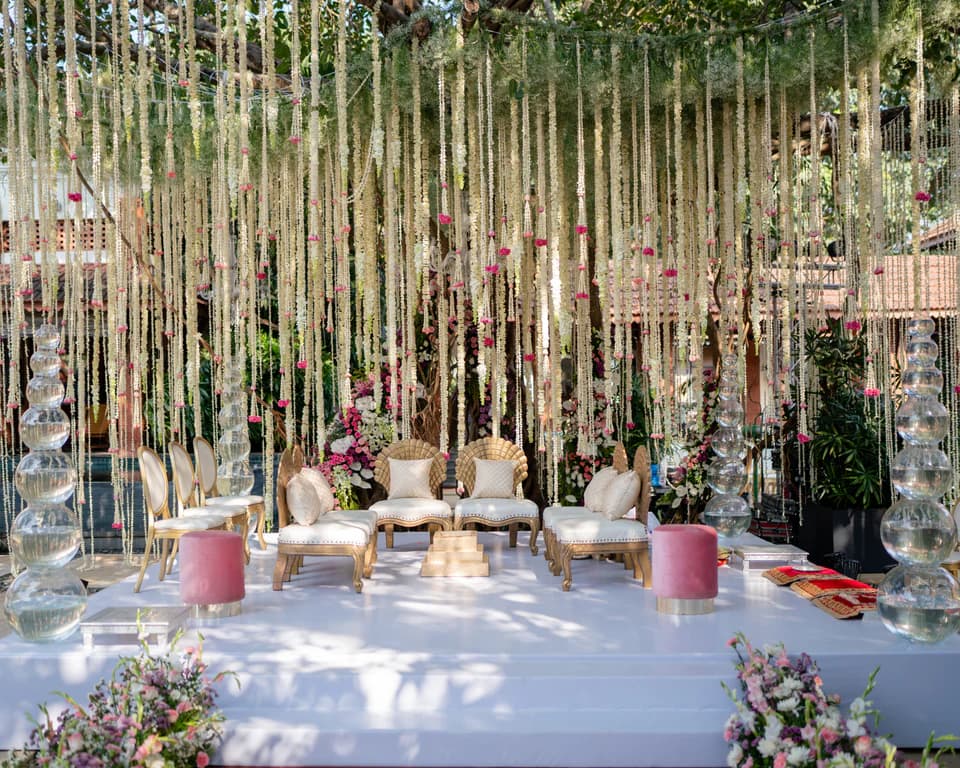 Wedding aisle beneath trees with hanging glass strands and white floral decor