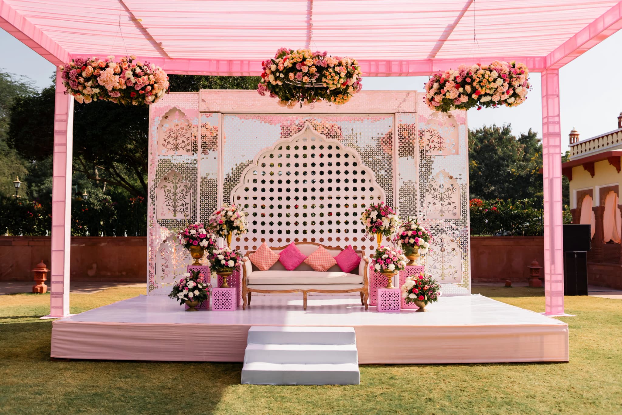 Blush-pink wedding stage beneath a translucent canopy in a garden