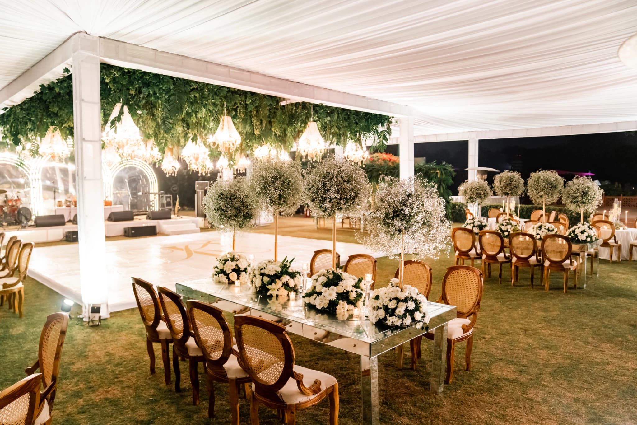 Elegant outdoor wedding dining beneath a white canopy and chandeliers
