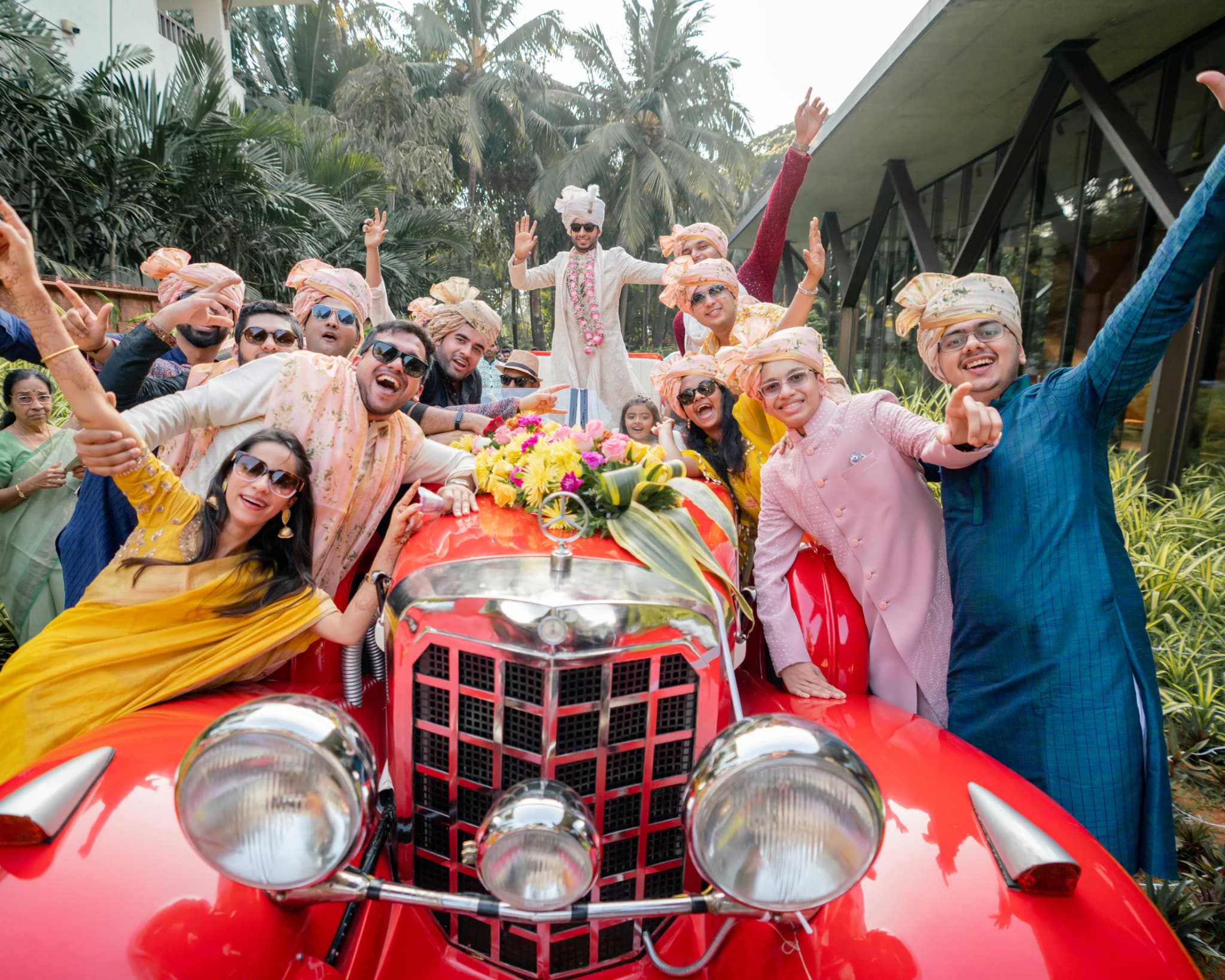Wedding guests celebrating around a red vintage convertible in a tropical setting