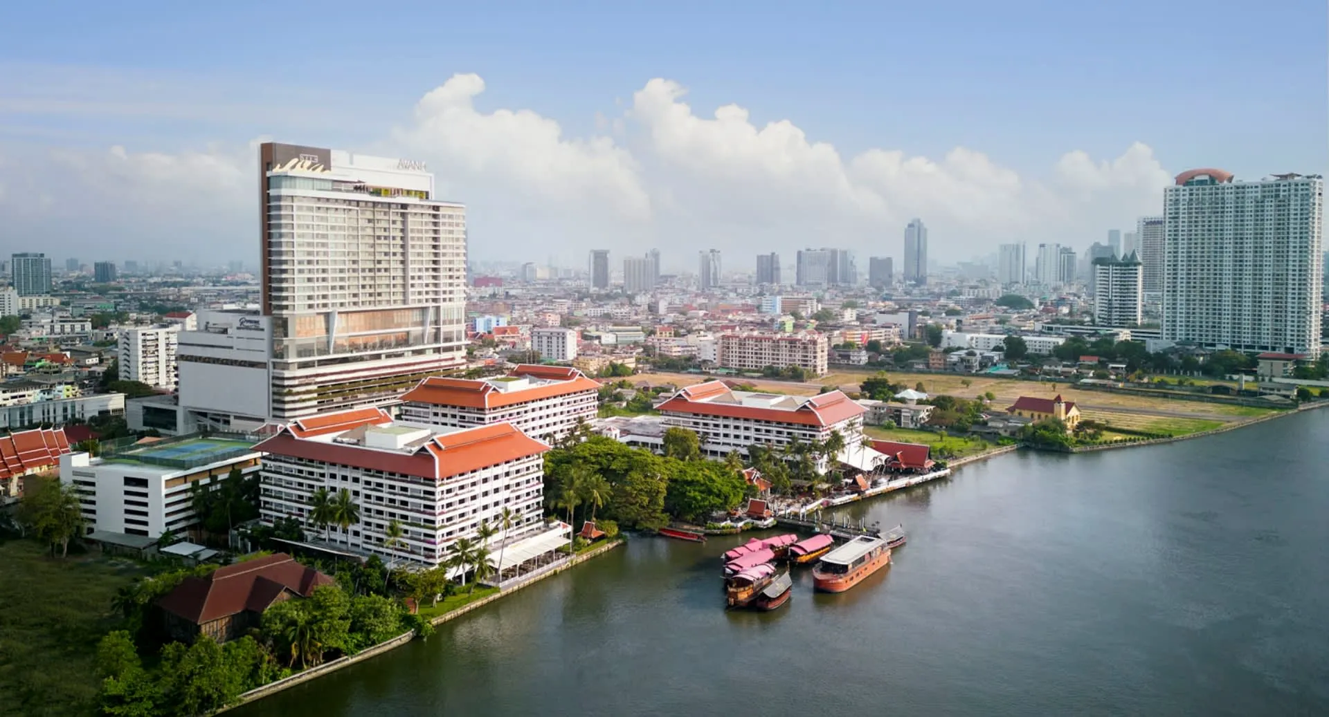 Aerial view of Anantara Riverside Bangkok Resort with 11 acres of riverfront gardens on the west bank of the Chao Phraya River, Bangkok skyline beyond