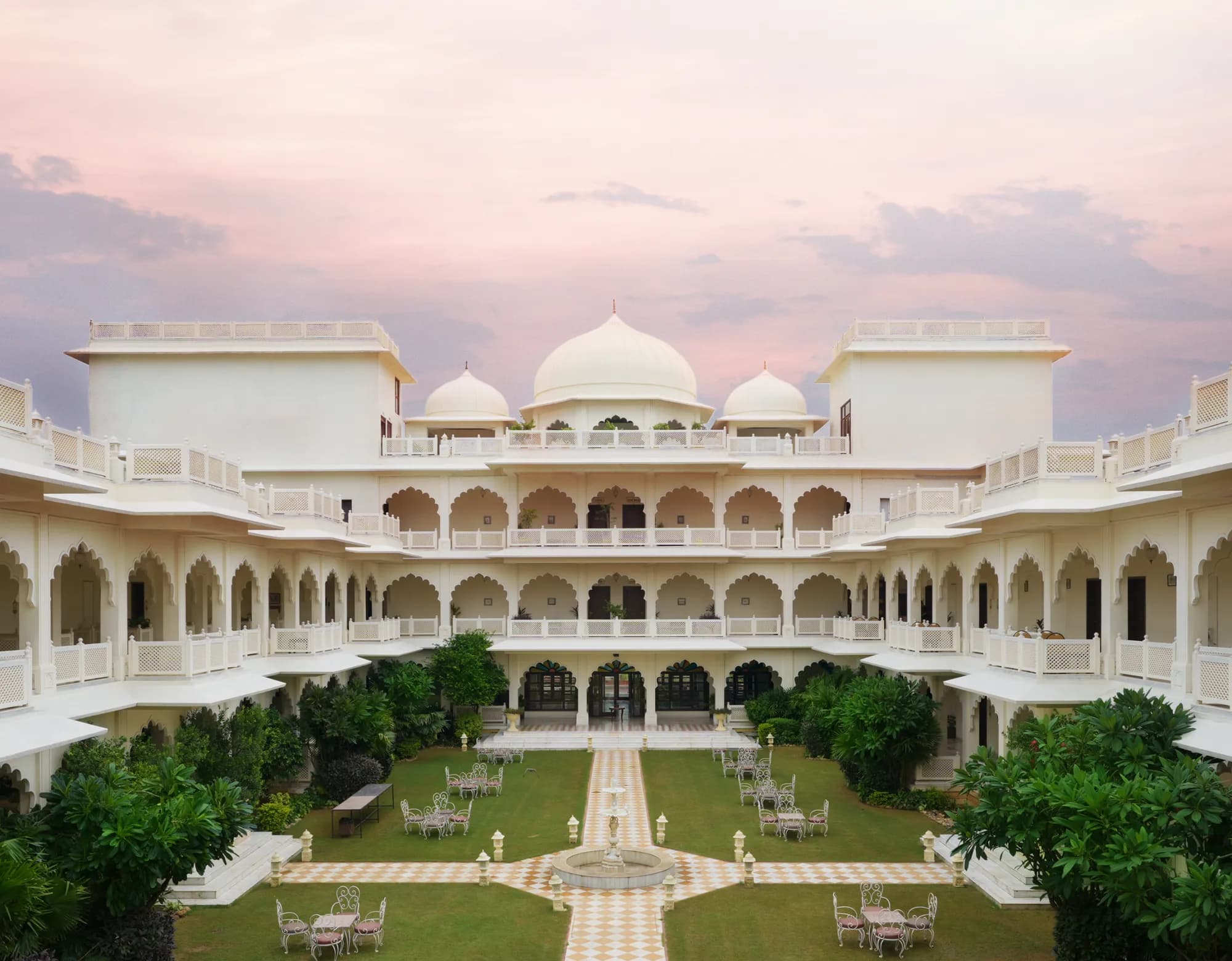 All-white Rajasthani haveli facade of Anuraga Palace Ranthambore with carved arches and jharokhas above green lawns