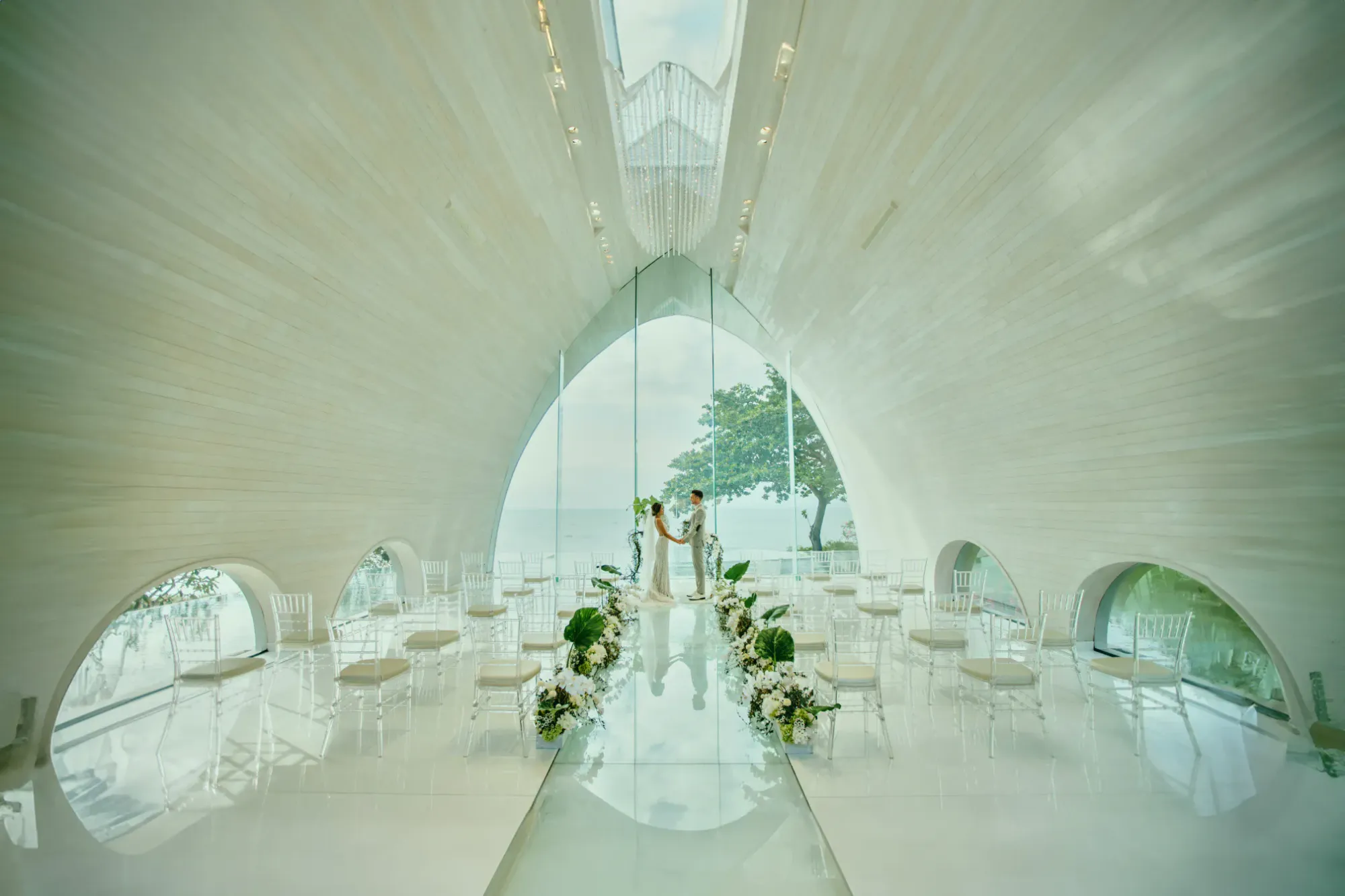 Interior of the translucent white glass Tresna Chapel with a water aisle above the Indian Ocean at AYANA Estate Bali