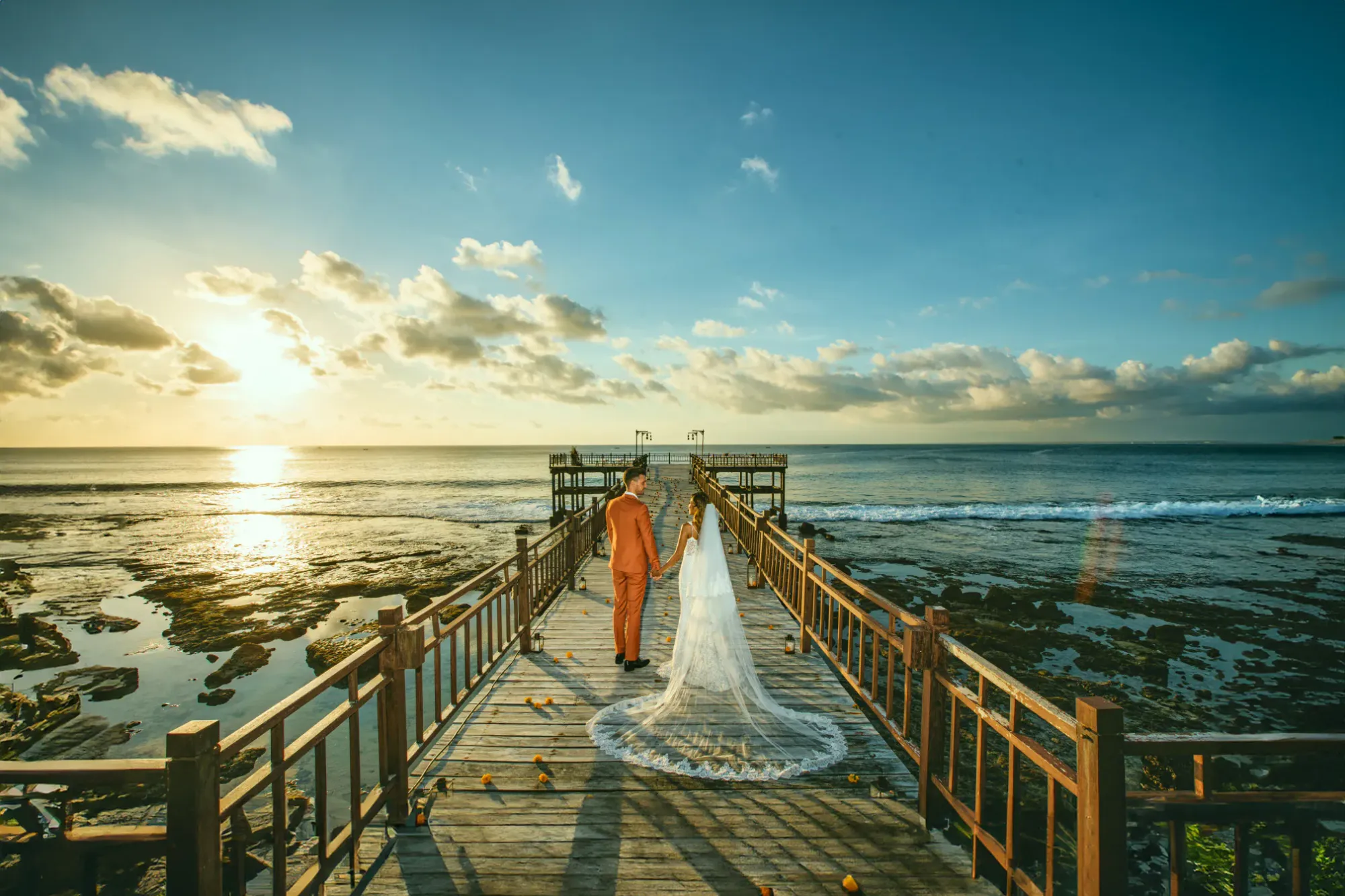 Couple on the wooden KISIK pier over the water at sunset at AYANA Estate Bali, Jimbaran