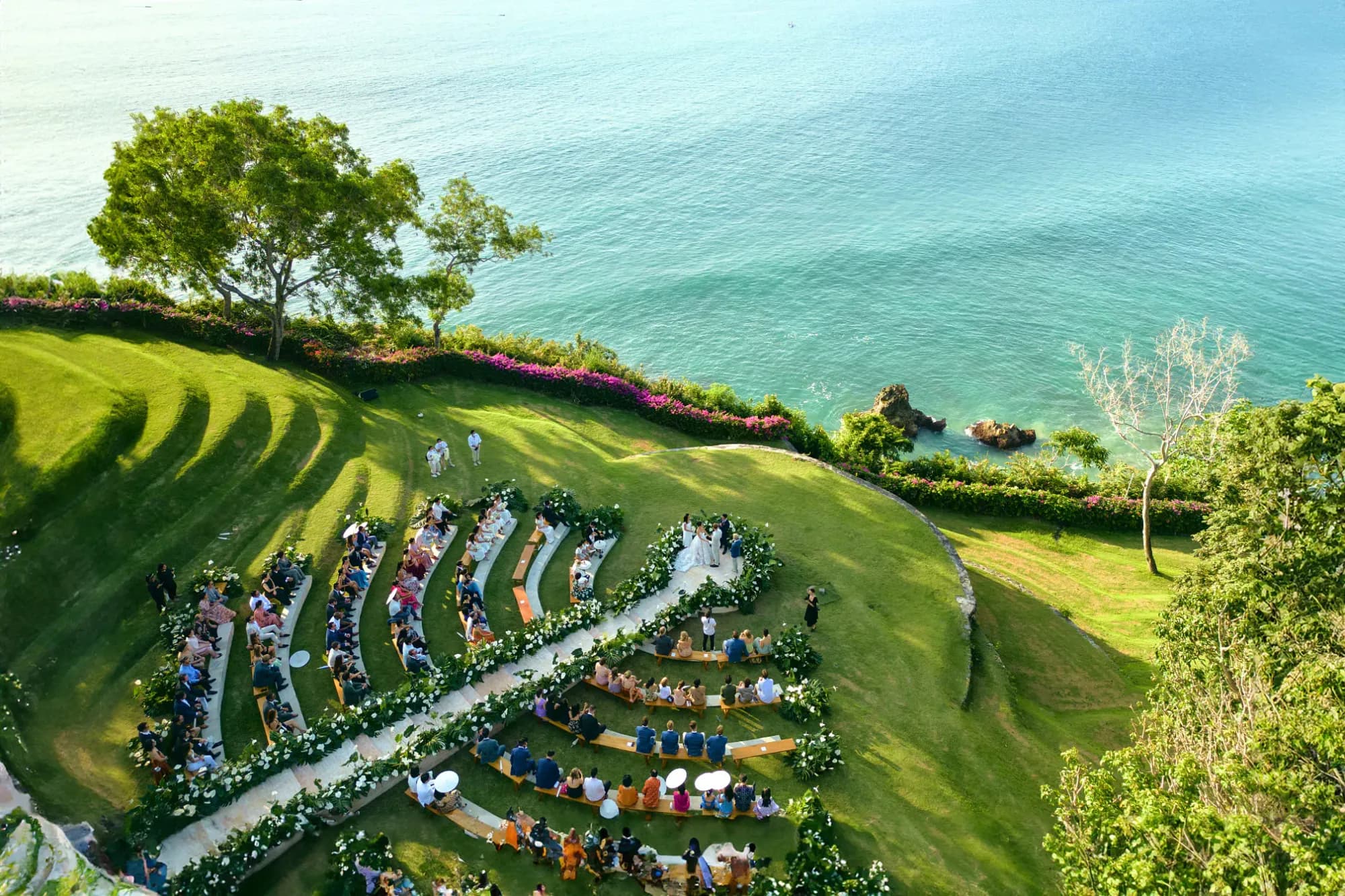 Aerial of AYANA Estate Bali clifftop lawns set for a wedding on green terraces above the turquoise Indian Ocean, Jimbaran