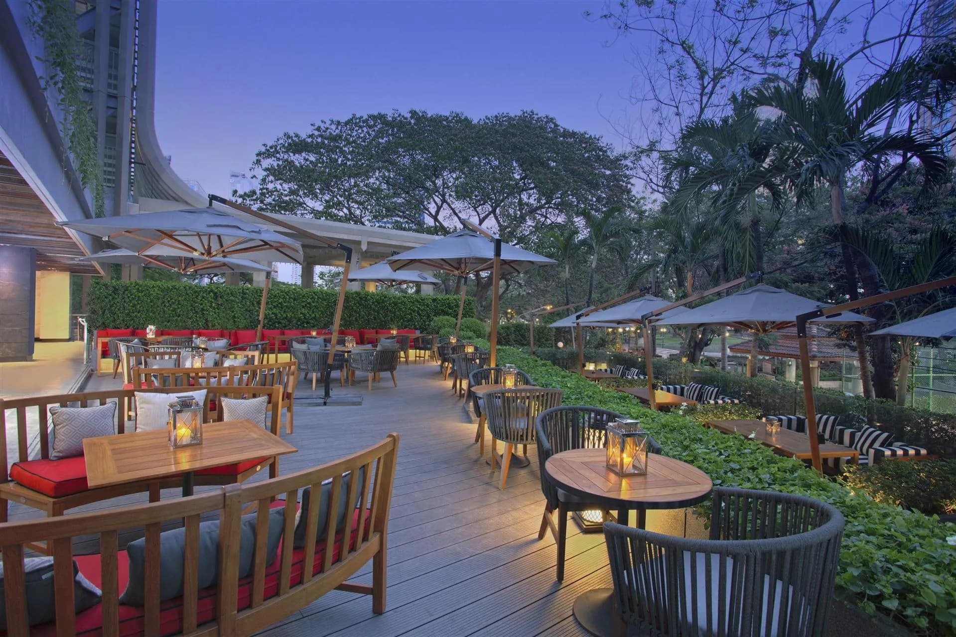 Outdoor garden terrace with umbrellas and greenery at dusk at Bangkok Marriott Marquis Queen's Park