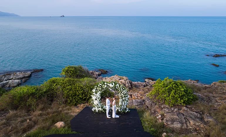 Cape Fahn wedding ceremony couple beneath a white floral arch on the headland deck with the Gulf of Thailand behind