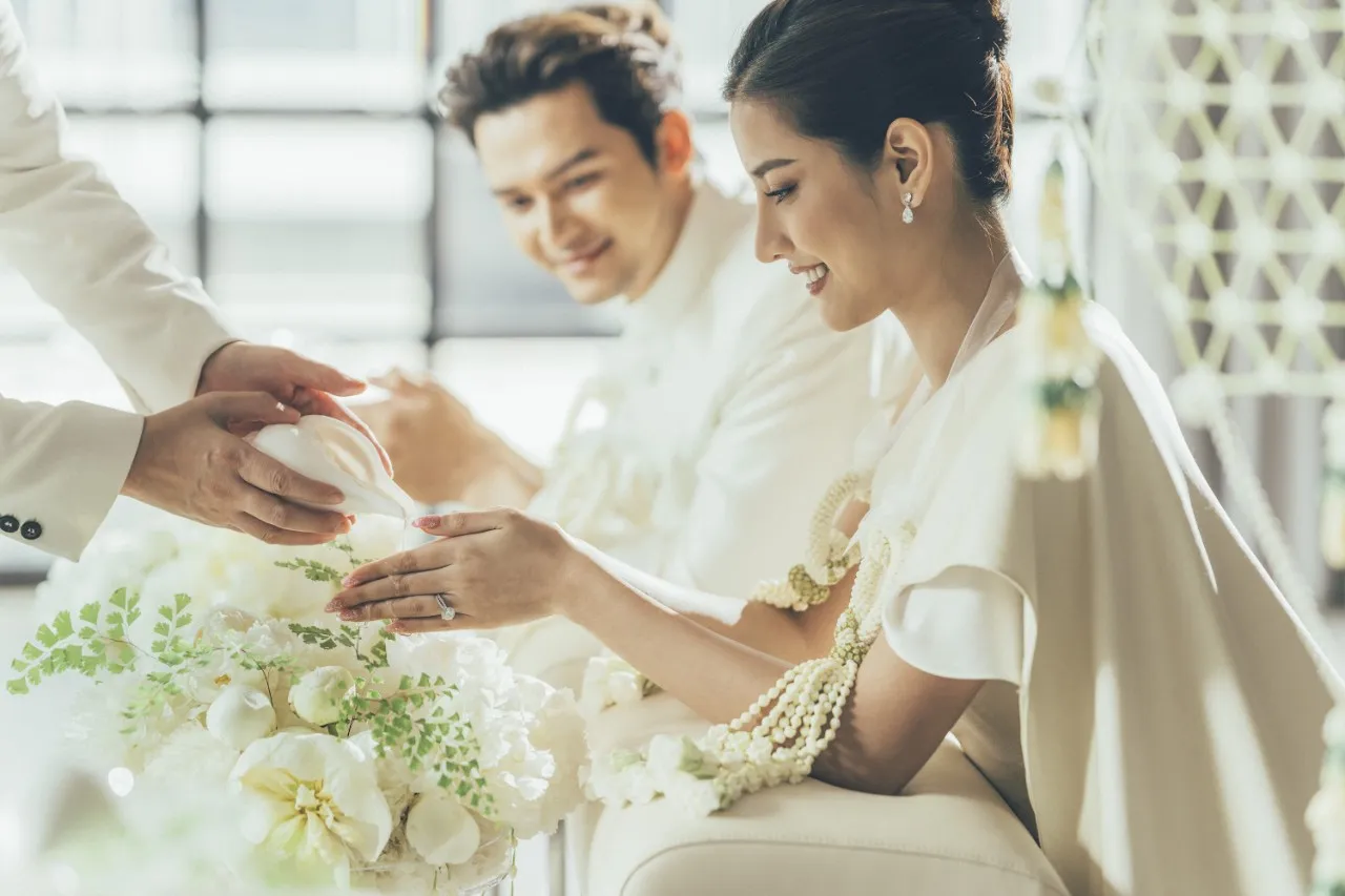 Couple in white during a ceremony water-pouring ritual with white florals at Four Seasons Hotel Bangkok