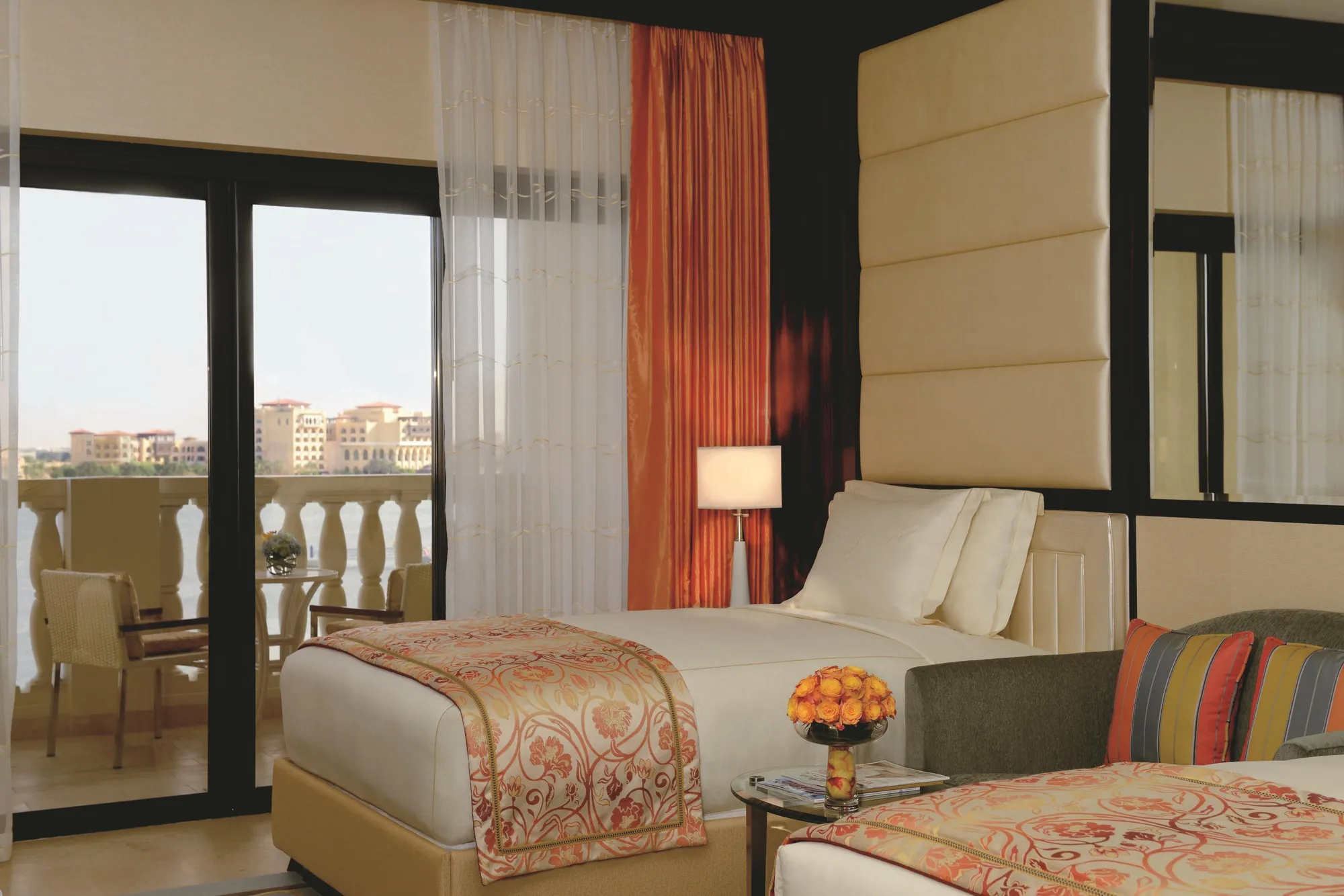 Guest room with twin beds, orange drapes and a canal-view balcony at The Ritz-Carlton Abu Dhabi Grand Canal