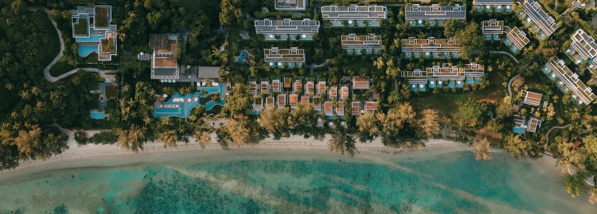 Rosewood Phuket resort pool with wooden bridges and palms beside the Emerald Bay beach