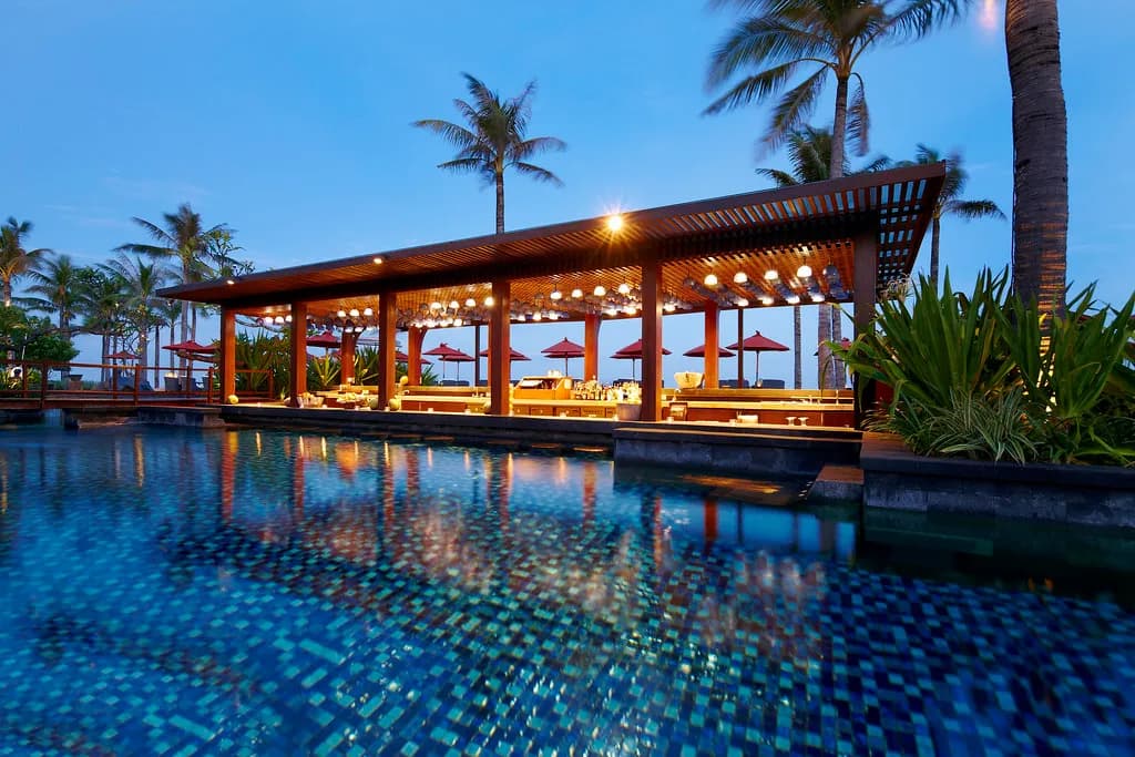 Vista Bar pavilion lit at dusk over the saltwater lagoon pool with palms at The St. Regis Bali Resort, Nusa Dua