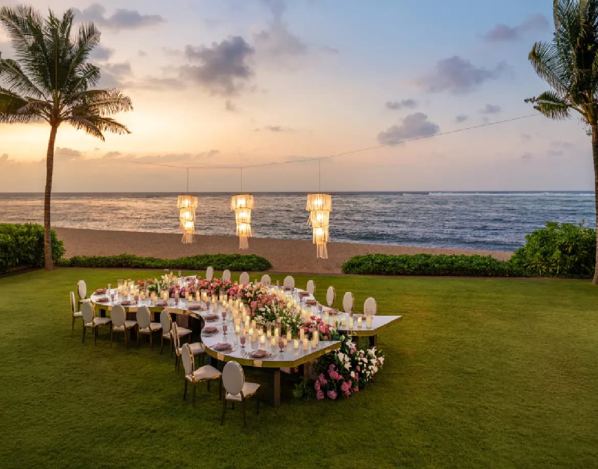 Beachfront lawn reception with floral table and hanging chandeliers at sunset beside the Indian Ocean at The St. Regis Bali Resort, Nusa Dua