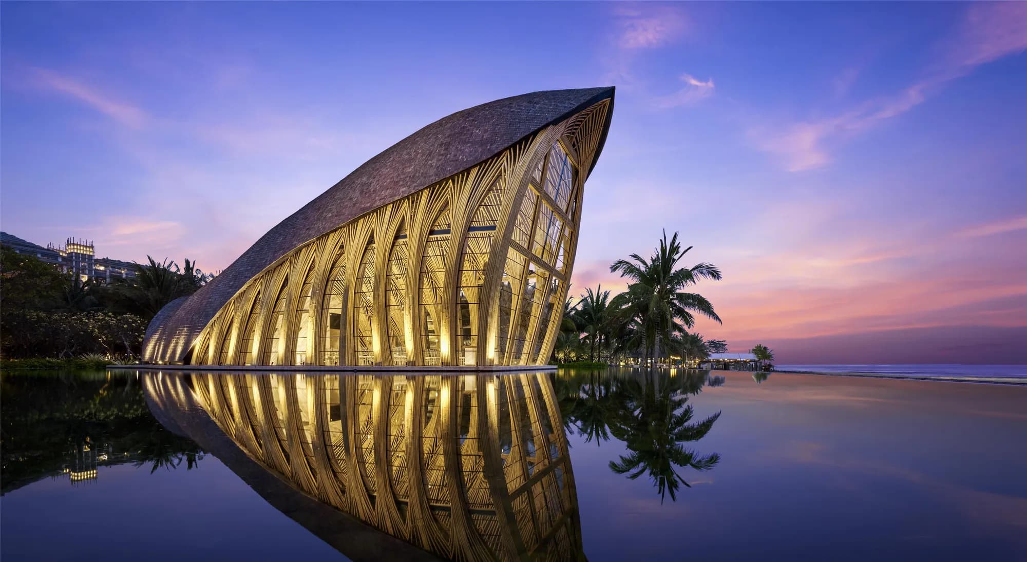 The glass Ocean Front Apurva Chapel illuminated over the water at dusk at The Apurva Kempinski Bali, Bali