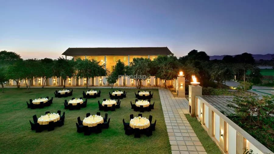 Outdoor lawn reception set with round dinner tables at dusk, building lit behind, The Westin Pushkar Resort & Spa