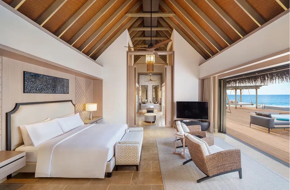 Over-water villa bedroom interior with vaulted thatched ceiling opening onto the pool deck at Waldorf Astoria Maldives Ithaafushi