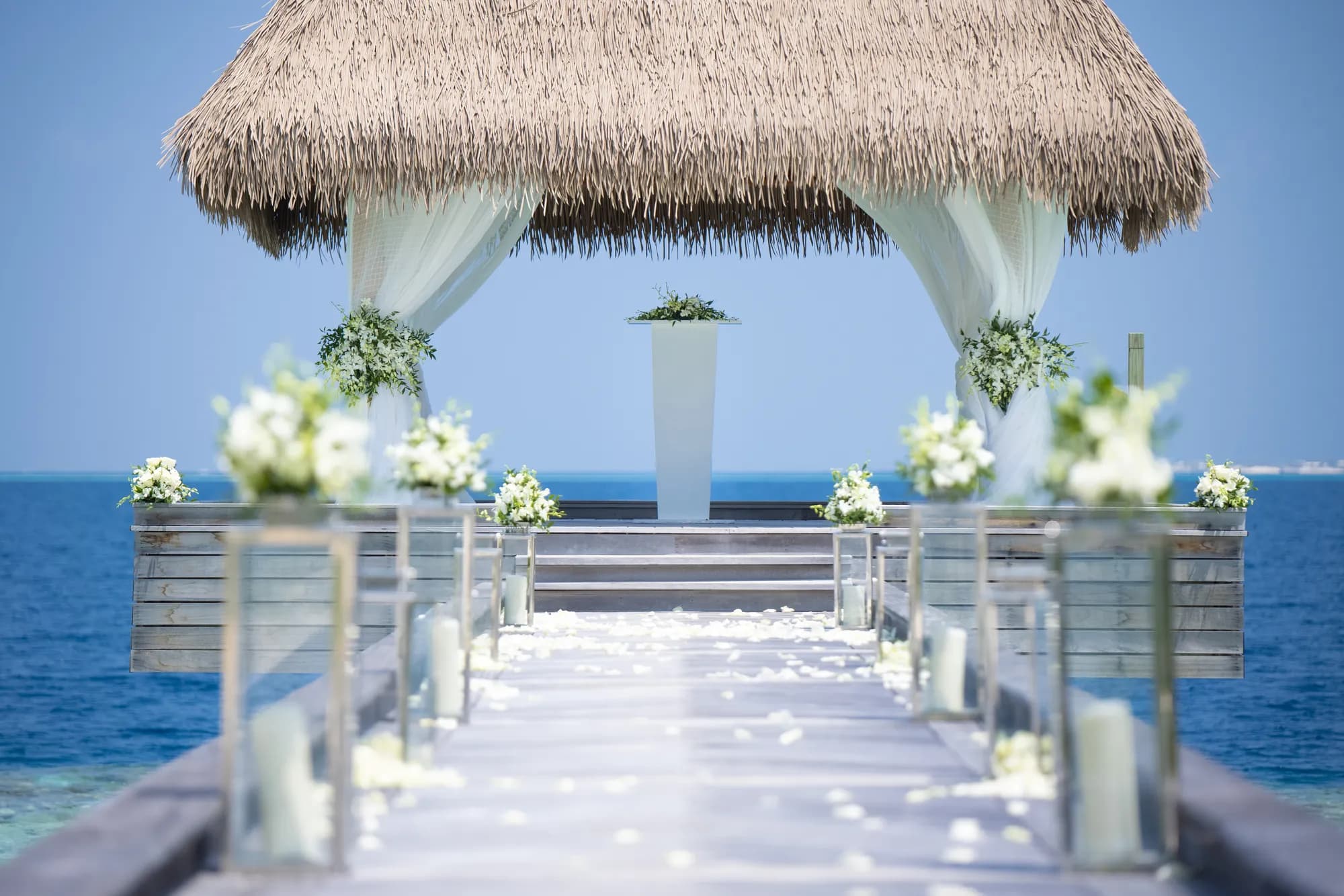 Over-water Wedding Pavilion dressed with white florals and a petal-strewn jetty for a ceremony at Waldorf Astoria Maldives Ithaafushi