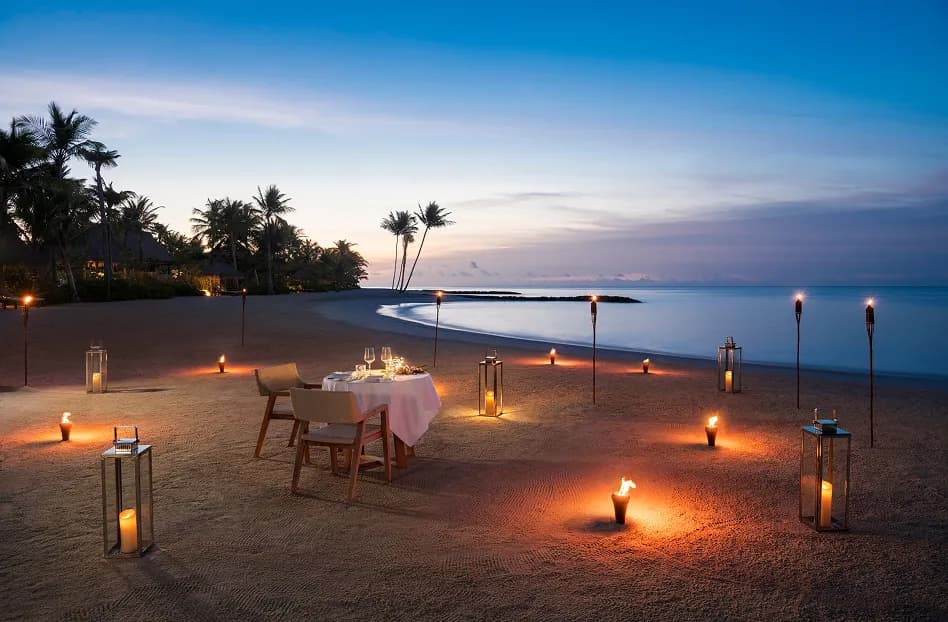 Candle-lit private beach dinner with lanterns and torches at dusk at Waldorf Astoria Maldives Ithaafushi