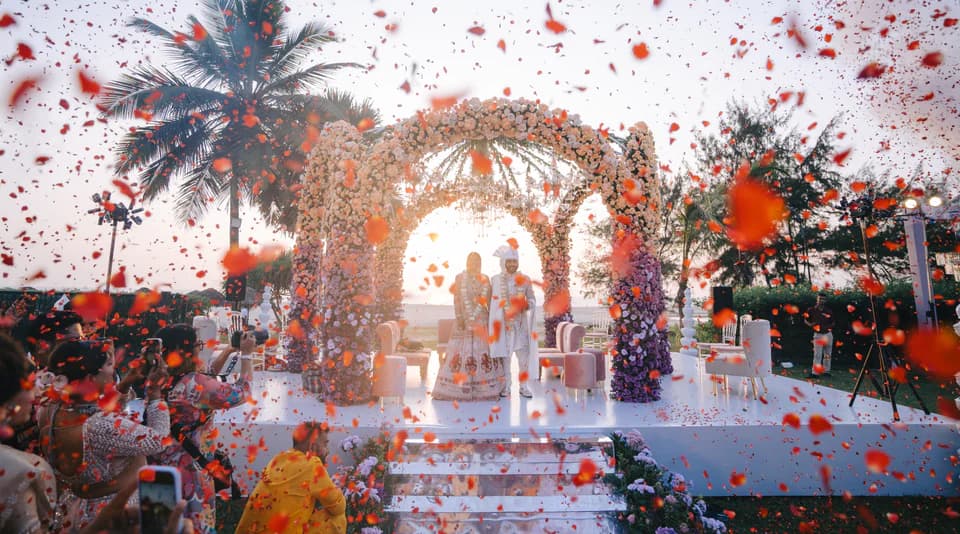 Wedding couple beneath a floral ceremony arch surrounded by falling red petals