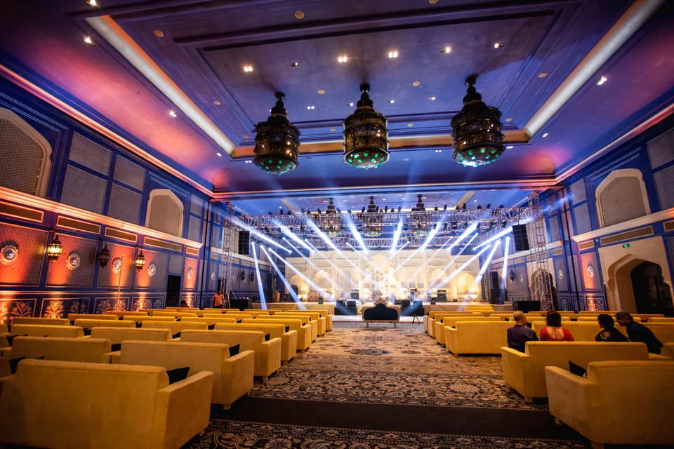 Large wedding ballroom with blue lighting, lounge seating, and a performance stage