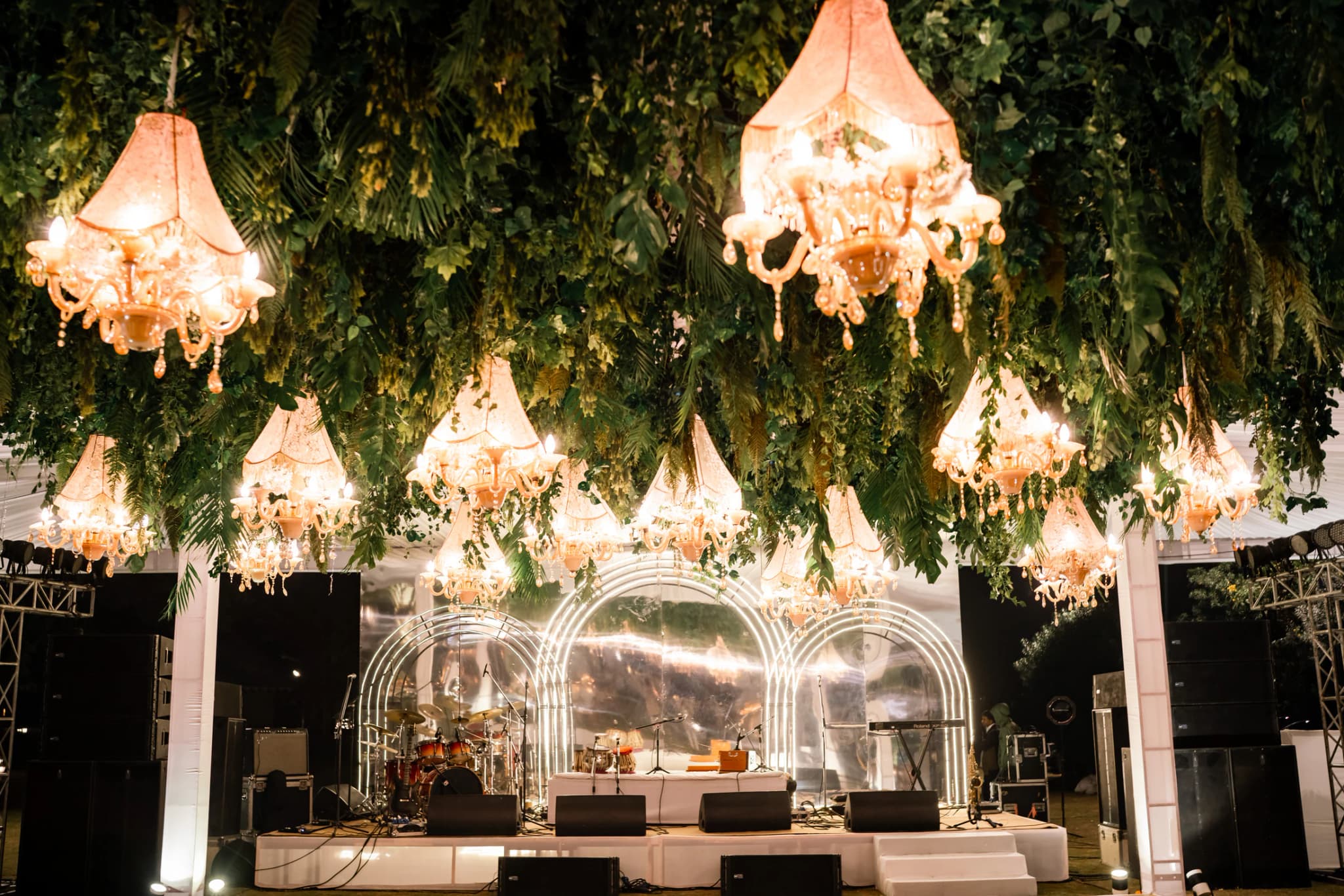 Outdoor wedding reception with chandeliers suspended from trees above a glowing stage