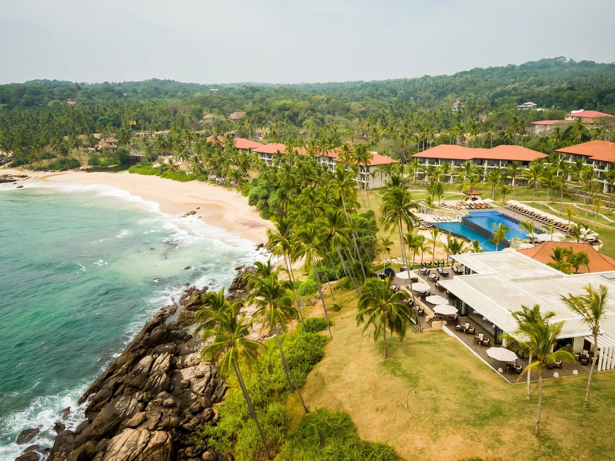 Aerial view of Anantara Peace Haven Tangalle clifftop headland with coconut palms, golden beach and the Indian Ocean, Sri Lanka