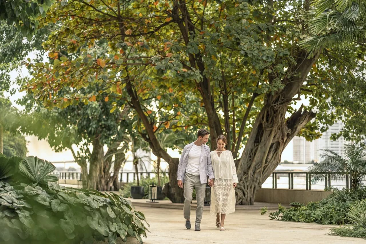 Couple walking a landscaped riverside garden promenade beside the Chao Phraya River at Four Seasons Hotel Bangkok