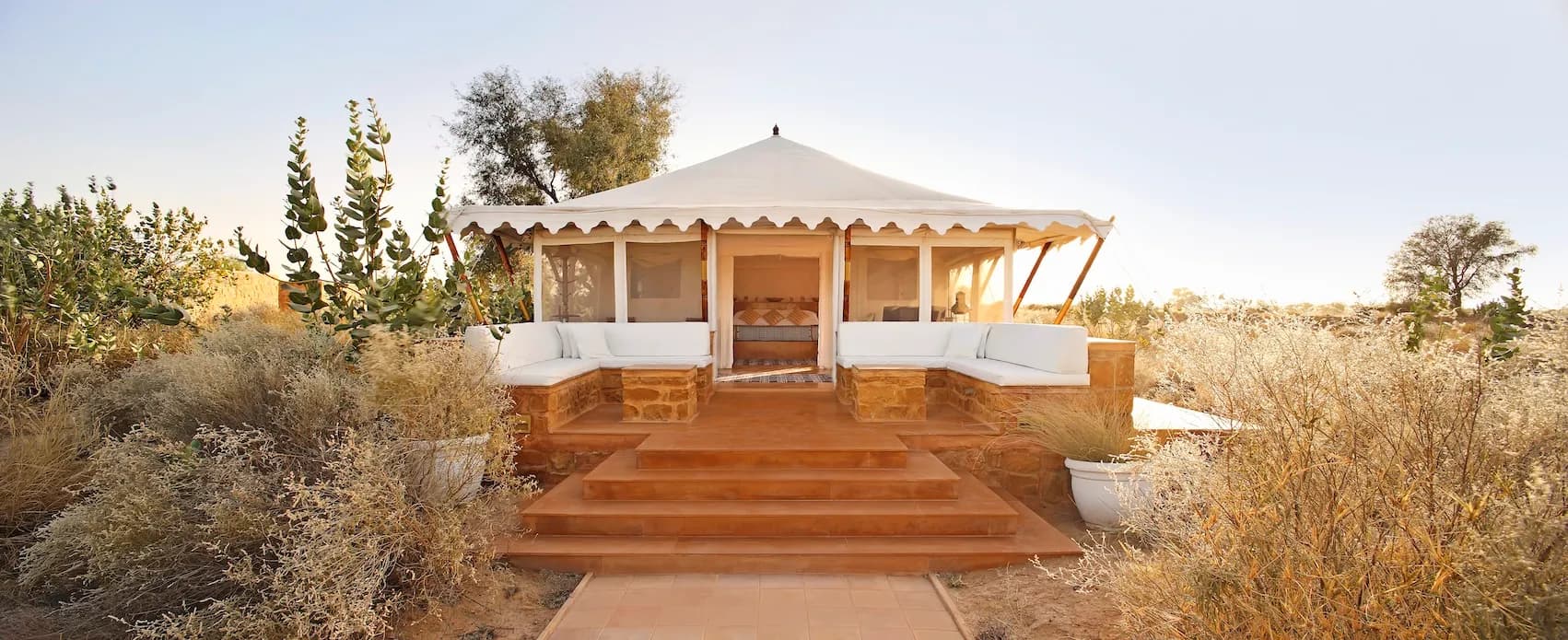 White canvas tented suites raised on honey-hued sandstone plinths across the Thar Desert estate at SUJÁN The Serai
