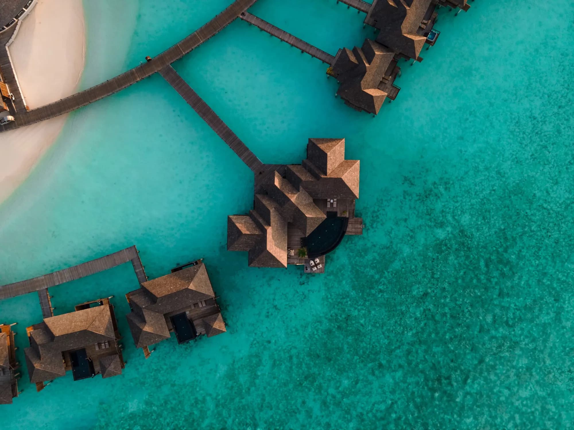 Aerial view of Sun Siyam Iru Fushi private island and over-water villas ringed by turquoise lagoon in Noonu Atoll, Maldives