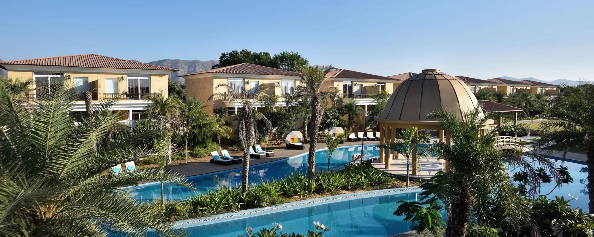 The Westin Pushkar Resort & Spa villas, lagoon-style pool and lit dome pavilion with the Aravalli hills behind, Pushkar