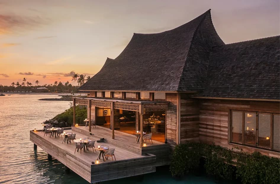 Over-water dining pavilion lit at sunset on the deck above the lagoon at Waldorf Astoria Maldives Ithaafushi