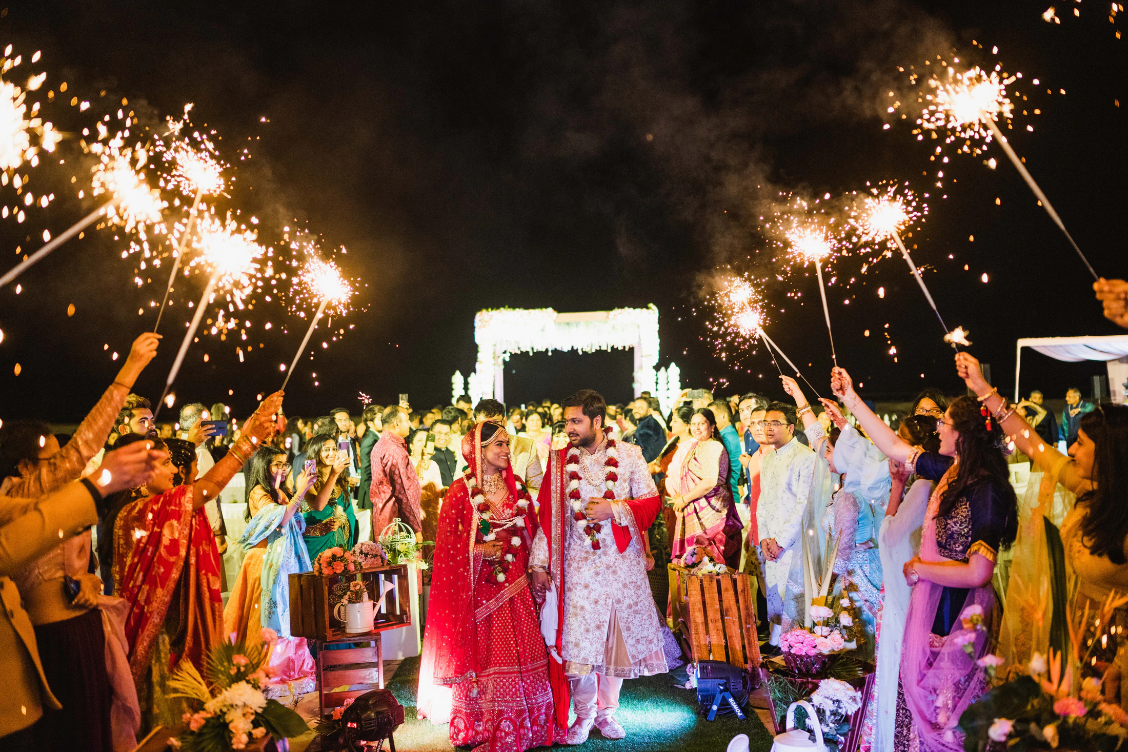 Newlyweds walking through cheering guests holding sparklers at night