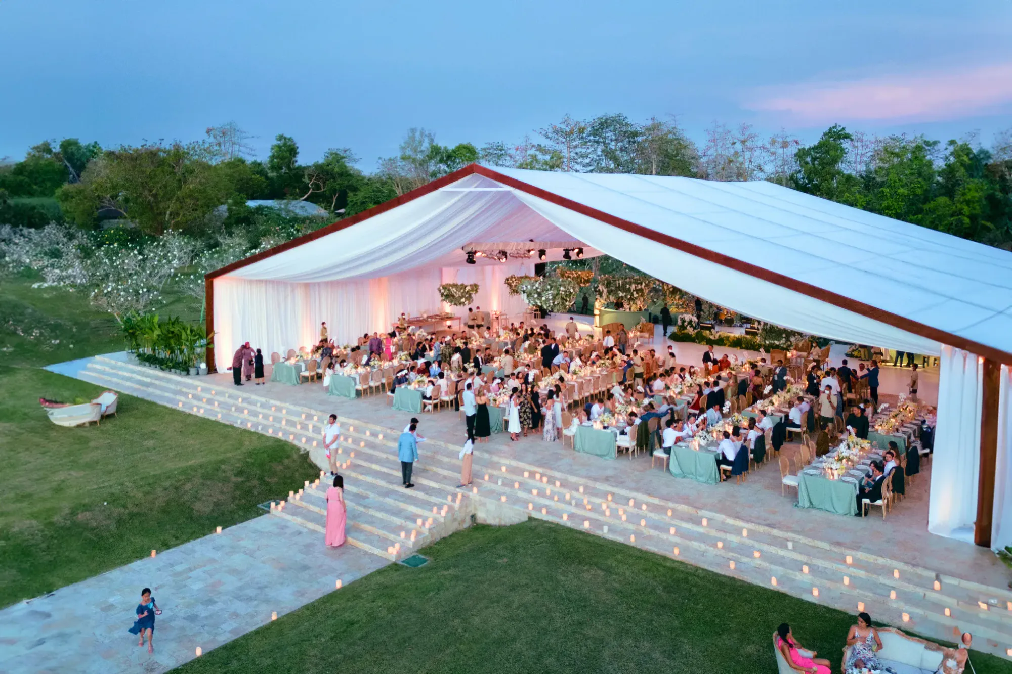 Large open-air reception with guests in Champa Garden at dusk at AYANA Estate Bali, Jimbaran