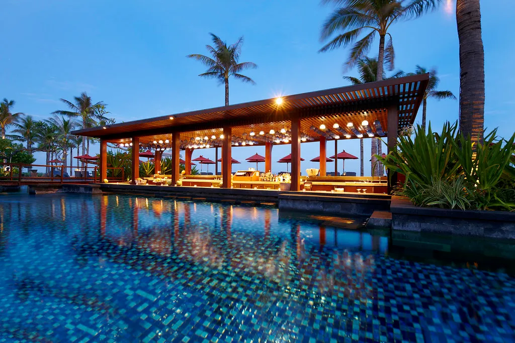 Vista Bar pavilion lit at dusk over the saltwater lagoon pool with palms at The St. Regis Bali Resort, Nusa Dua