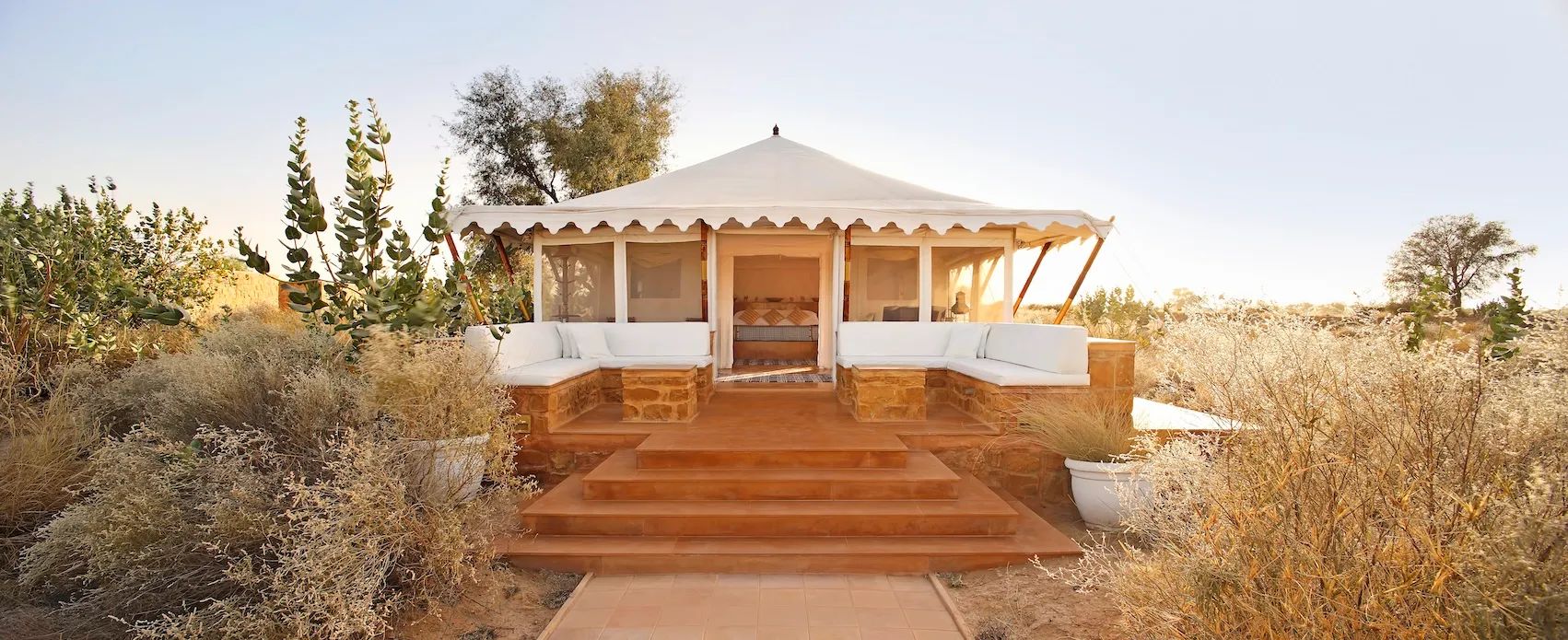 White canvas tented suites raised on honey-hued sandstone plinths across the Thar Desert estate at SUJÁN The Serai