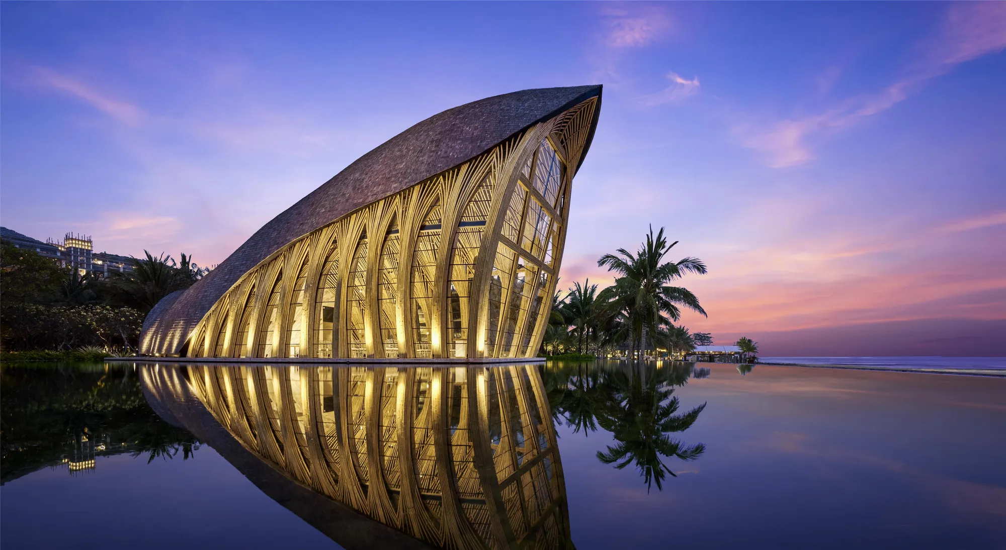 The glass Ocean Front Apurva Chapel illuminated over the water at dusk at The Apurva Kempinski Bali, Bali