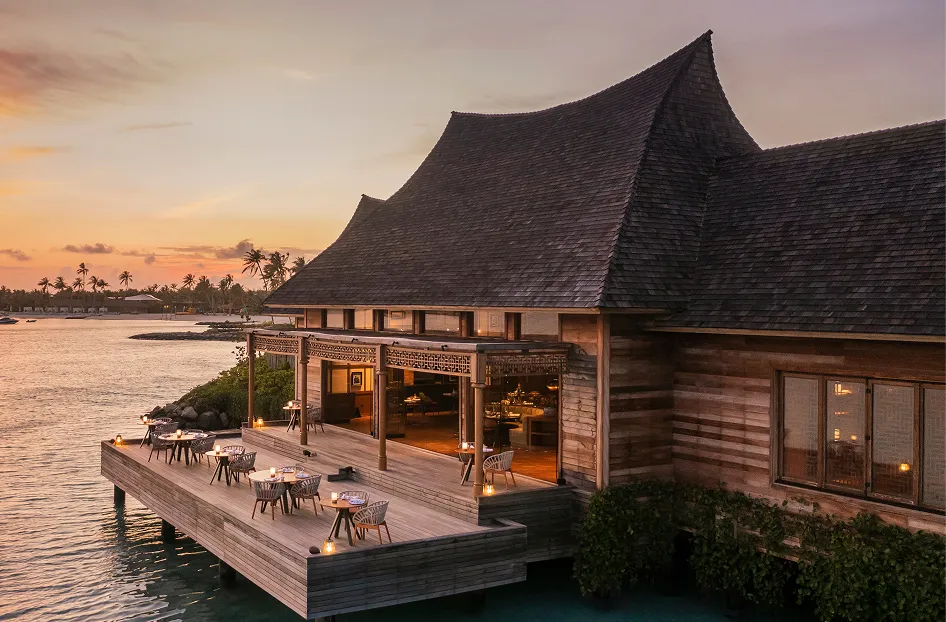 Over-water dining pavilion lit at sunset on the deck above the lagoon at Waldorf Astoria Maldives Ithaafushi