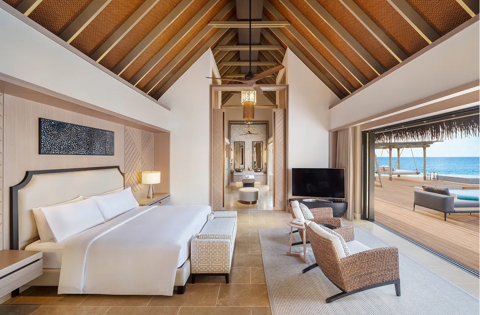 Over-water villa bedroom interior with vaulted thatched ceiling opening onto the pool deck at Waldorf Astoria Maldives Ithaafushi