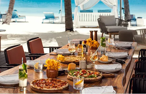 Beachfront dining table set with food and flowers on the sand beside a cabana at Waldorf Astoria Maldives Ithaafushi