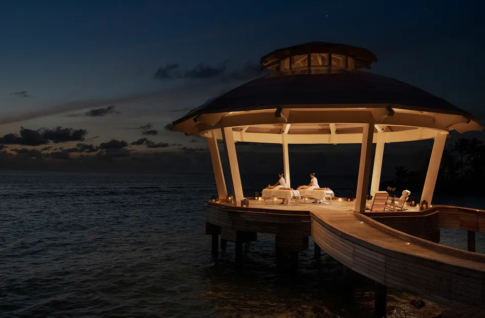 Thatched over-water pavilion lit with lanterns along the jetty against the Indian Ocean at dusk, Waldorf Astoria Maldives Ithaafushi